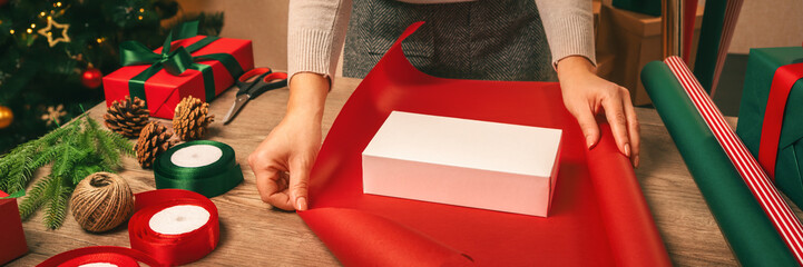 A Christmas gift wrapped in bright red wrapping paper. Nearby are satin ribbons, scissors, fir...