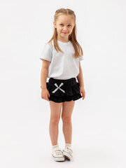Fototapeta premium A modest Caucasian girl with a kind smile and slender legs is standing on a white background. She is wearing a T-shirt, a skirt, and sneakers.