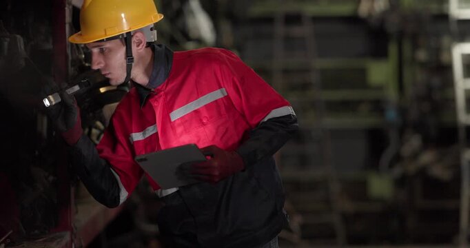 A warehouse technician uses a flashlight and tablet to examine used automotive parts on dim shelves, conducting quality and inventory checks.
