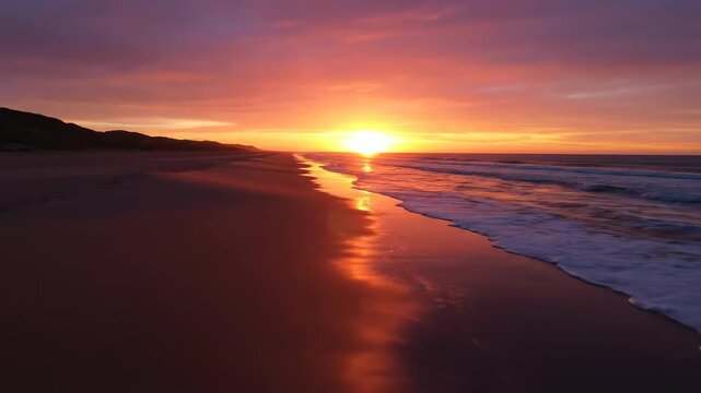 A beautiful orange sunset on the beach casts a warm light reflecting over the ocean waves and sandy coast under a dramatic summer sky