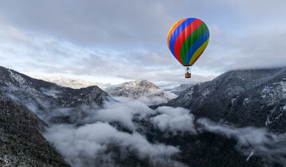 Colorful Hot Air Balloon Over Snowy Mountain Valley With Clouds in Aerial Adventure