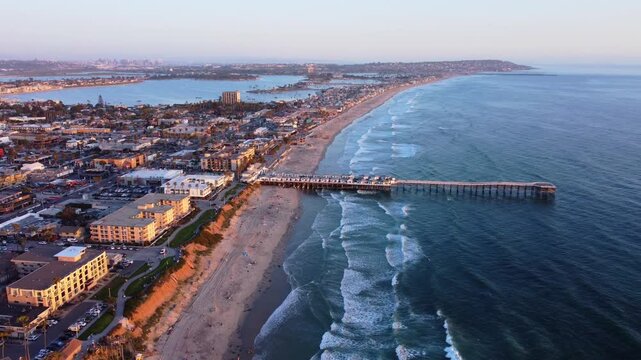 Pacific Beach Township, Sunset at Pier, looking towards San Diego skyline, Southern California. Drone view of sandy shores, beachfront buildings, bike path, and nearby houses in coastal neighbourhood