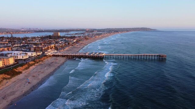Pacific Beach Sunset at Pier, looking towards San Diego skyline, Southern California. Aerial drone view of sandy shores, beachfront buildings, bike path, and pier on a nice warm summer evening.