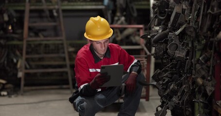 Male technician uses a barcode scanner and digital tablet to inspect and check the inventory of automotive parts on warehouse shelves, ensuring accurate stock management and quality control