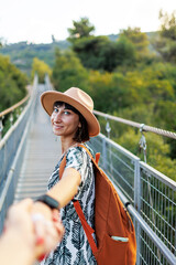 Fototapeta premium girl in a hat walks along a suspension bridge. Autumn season outdoors, portrait of a woman walking on a suspension bridge over a river.