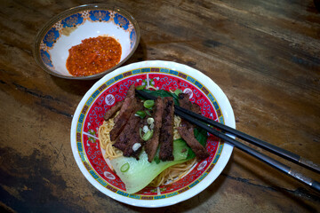 A bowl of ramen noodle and sliced cow meats, Japanese food with black chopsticks on a wooden table