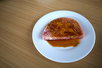 Fresh raw beef on a white plate ready to be grilled, on a wooden table
