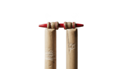 Closeup of two wooden cricket stumps with bright red bails balanced on top, detailed wicket equipment isolated on white background symbolizing dismissal, bowled and run out moments

