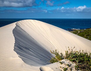 Large sand dune curving towards the sea under partly cloudy skies
