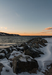 Winter Shoreline with Snow-Covered Rocks and Jetty at Dusk