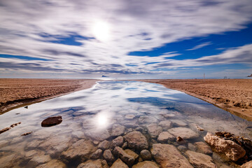 Vibrant Beach Inlet Reflection Under Streaked Sky