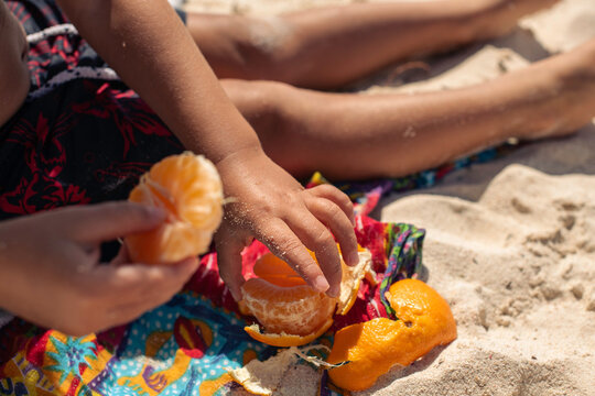 Child sitting in sand eating an orange at beach