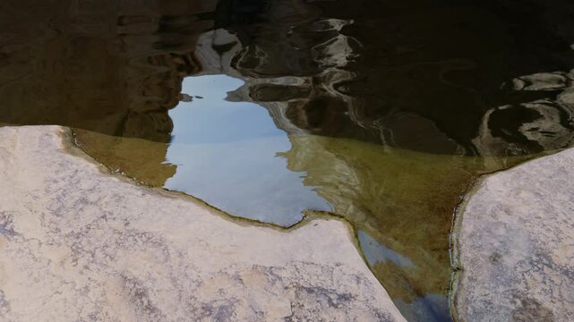 Smooth pan from a still pool to towering limestone cliffs and a seasonal dry waterfall in Ein Avdat Nature Reserve, Negev desert, Israel. Quiet oasis mood and rugged geology
