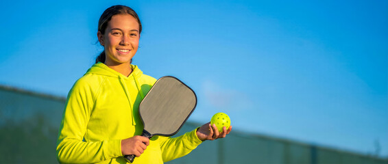 Young woman with a racket and pickleball ball on a court, copy space for an advertisement for a popular ball game