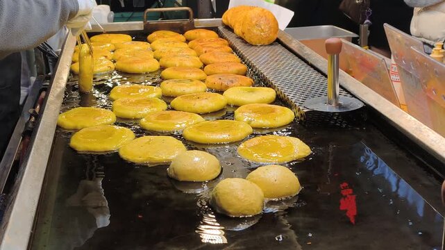 Korean cuisine highlights traditional sweet snacks. Vendor deep fries traditional snacks carefully. Korean cuisine offers unique market tastes. Concept of street food in Asia.