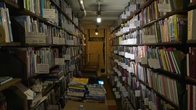 There are many books in the book depository of the old library. There are shelves with books on the sides.