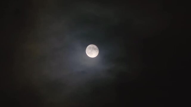 A full moon in a cloudy night sky. Translucent clouds surround the moon
