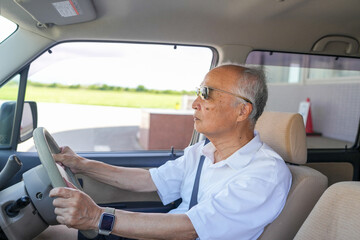 A man in a white shirt is driving a car with a steering wheel. He is wearing sunglasses and a watch