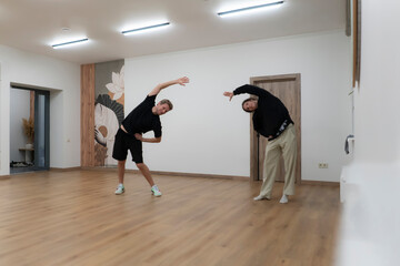 Two individuals are stretching their bodies in a spacious room at night
