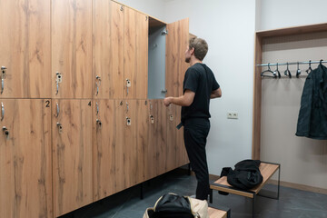 A man looks inside a locker in a gym changing room while standing next to benches