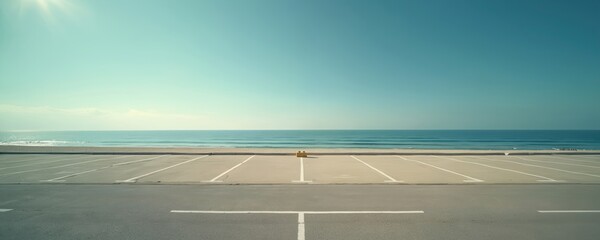 Empty parking lot borders vast blue ocean under clear sky. Sun shines bright on quiet beachside. No cars present near calm sea waves. Peaceful seascape backdrop.