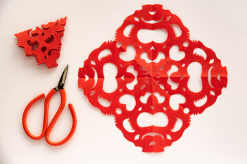 Red paper cutouts,scissors,and a triangular piece on white background.