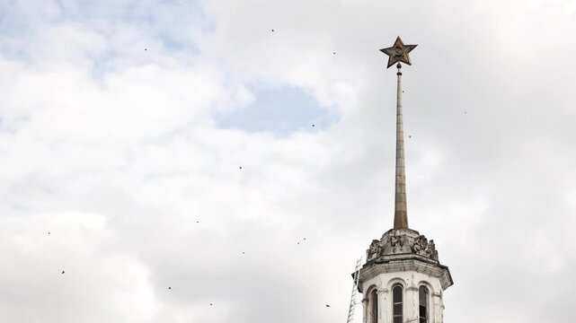 Soviet star and hammer and sickle atop a historical building spire against cloudy sky in Moscow.