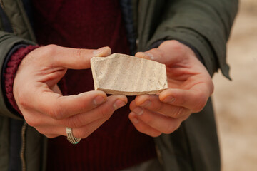 A close-up of a piece of textured pottery. Historical. From the city of Rey, Iran, it is brightly colored with ancient reliefs and markings, showing the hands of the person holding it.