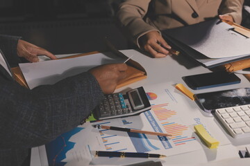 business documents on office table with tablet, smart phone and laptop and two colleagues discussing data