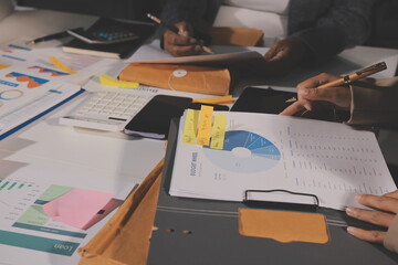 business documents on office table with tablet, smart phone and laptop and two colleagues discussing data