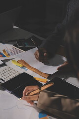 business documents on office table with tablet, smart phone and laptop and two colleagues discussing data