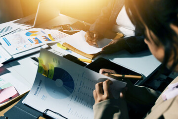 business documents on office table with tablet, smart phone and laptop and two colleagues discussing data