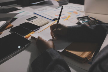 business documents on office table with tablet, smart phone and laptop and two colleagues discussing data