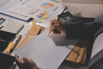 business documents on office table with tablet, smart phone and laptop and two colleagues discussing data