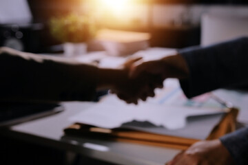 Entrepreneurs collaboration deal shaking hands in a modern office and financial paper graph on desk.
