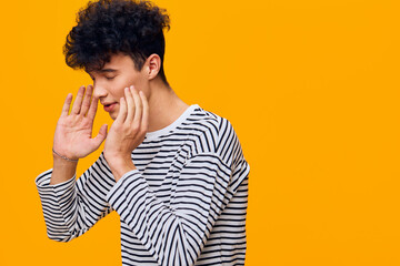 young man in striped shirt whispering with hands near mouth on bright orange background showing secretive gesture and focused facial expression