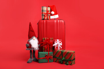 Suitcase with Santa hat, gifts and decorative dwarf on red background. Christmas vacation