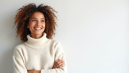 Young Black woman with curly hair smiles looking up thoughtfully wearing cozy knit sweater. Arms crossed, radiating warmth, contemplation in studio setting. Expression suggests pleasant surprise