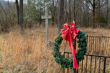 Christmas Wreath on Rusty Fence in Overgrown Cemetery with Cross