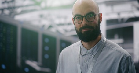 Focused IT Manager Supervising Modern Server Infrastructure. Bearded Male With Glasses and ID Badge Supervising Vast, Infrastructure of Data Center. Technology and Professional Oversight. Portrait.