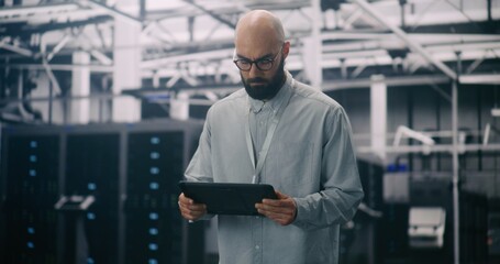 IT Professional Inspecting Racks in Data Center. Bearded Male Inspecting or Troubleshooting Equipment With Handheld Device Amidst Rows Data Servers. Concept Critical Maintenance and System Management.