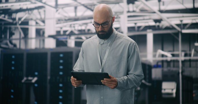 IT Professional Inspecting Racks in Data Center. Bearded Male Inspecting or Troubleshooting Equipment With Handheld Device Amidst Rows Data Servers. Concept Critical Maintenance and System Management. - Powered by Adobe