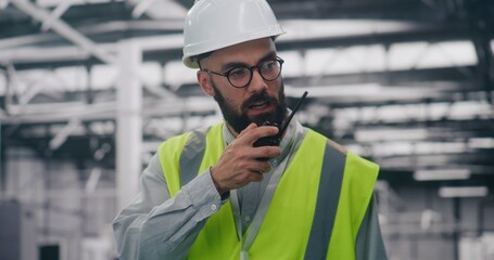 Industrial Management Engineer Directing Team With Radio. Specialist in Personal Protective Equipment Directs Personnel Using Radio in Large Industrial Setting. Management, Direction, Heavy Industry.