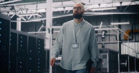 IT Engineer Walking Through Server Racks in Modern Data Center. Focused Man With Badge and Laptop Walking Among Rows of Glowing Server Racks. Concept of IT Infrastructure and Cloud Technology.