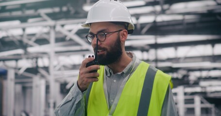 Safety Compliance Supervisor Reporting Conditions Via Two Way Radio. Focused Site Supervisor in Full Safety Gear Reports Work Conditions Using Two Way Radio In Facility. Concept Proactive Monitoring.