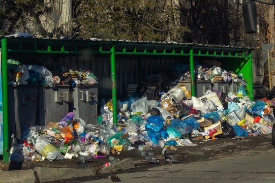Overfilled garbage bins with plastic waste bags on city street environmental pollution