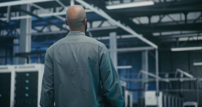 Engineer Walking Through Tech Enterprise Center. Bearded Professional Walking Steadily Through Brightly Lit Hall of Large Tech Enterprise Center. High Tech Work Environment and Maintenance Rounds.