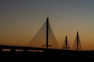 Fototapeta premium Mersey Gateway Bridge silhouetted against a warm sunrise sky above the River Mersey at low tide