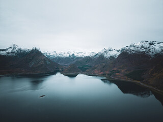 Calm Fjord Lake Reflecting Snowy Mountains Under an Overcast Sky in Northern Norway