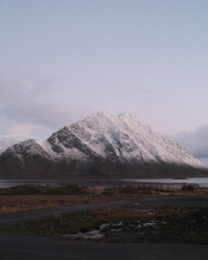 Snowy Mountain Rising Above Quiet Fjord With Road in Foreground at Nordic Twilight